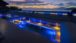 A modern hotel with a pool area, multiple balconies, and a view of the sea at dusk. - Fugaku Gunjo (Izu)