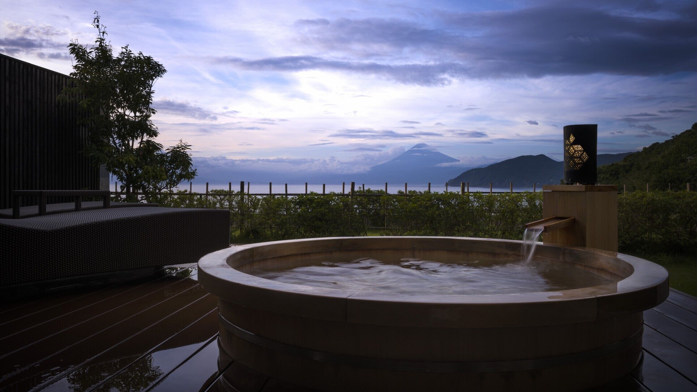 A hot tub on a wooden deck with a view of a mountain and a body of water.