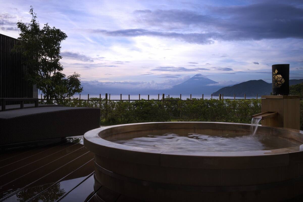 Un jacuzzi en una terraza de madera con vistas a una montaña y un cuerpo de agua.