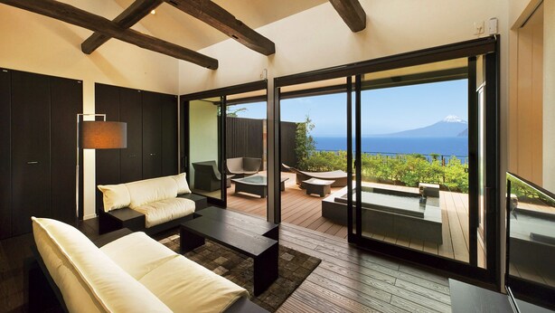 A modern interior with a sofa, coffee table, and a view of a mountainous landscape through large glass doors. - Fugaku Gunjo (Izu)