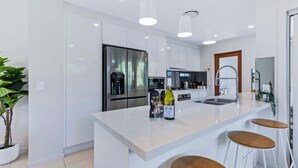 A modern kitchen with white cabinetry, stainless steel appliances, a central island with stools, and pendant lighting. - Park Avenue Luxe Chic Townhouse Sleeps 9, Carpark (Auchenflower)