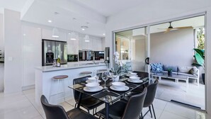 A modern kitchen with a central island, a dining area with a glass table, and a living space with a sofa and coffee table. - Park Avenue Luxe Chic Townhouse Sleeps 9, Carpark (Auchenflower)
