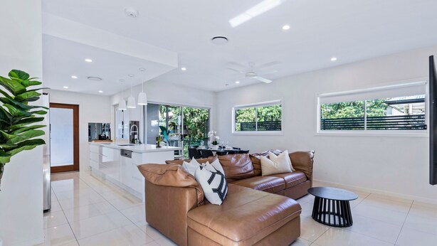 A modern living room with a brown leather sofa, a small round table, and a kitchen area in the background. - Park Avenue Luxe Chic Townhouse Sleeps 9, Carpark (Auchenflower)