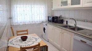 Cocina compacta con lavadora, lavaplatos y zona de comedor con mesa y sillas.