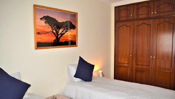 Un dormitorio con dos camas, un amplio armario de madera y un cuadro con un atardecer en la pared.