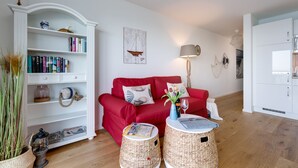 Een woonkamer met een rode bank, een witte boekenkast en rieten bijzettafeltjes.