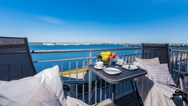 Een balkon met een tafel gedekt voor twee personen, met uitzicht op een waterpartij en een pier in de verte.