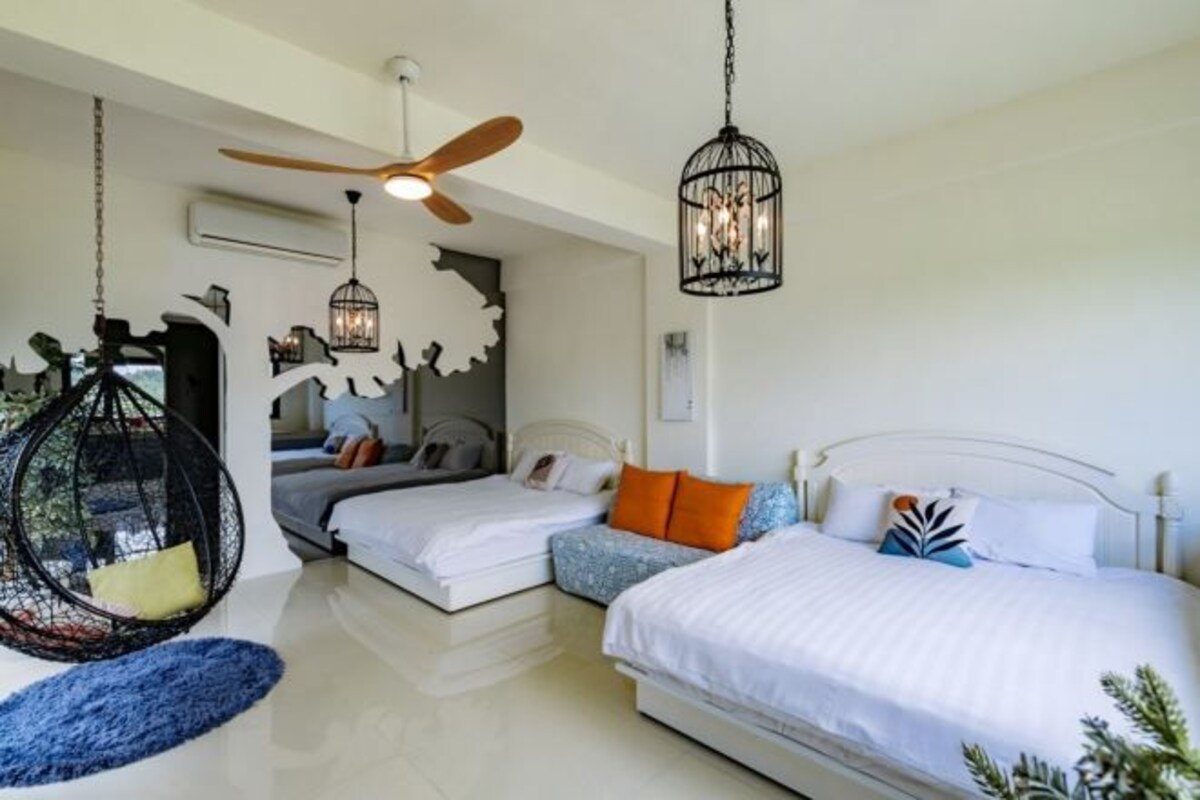 Un dormitorio con dos camas, una silla colgante, un ventilador de techo y una lámpara decorativa.