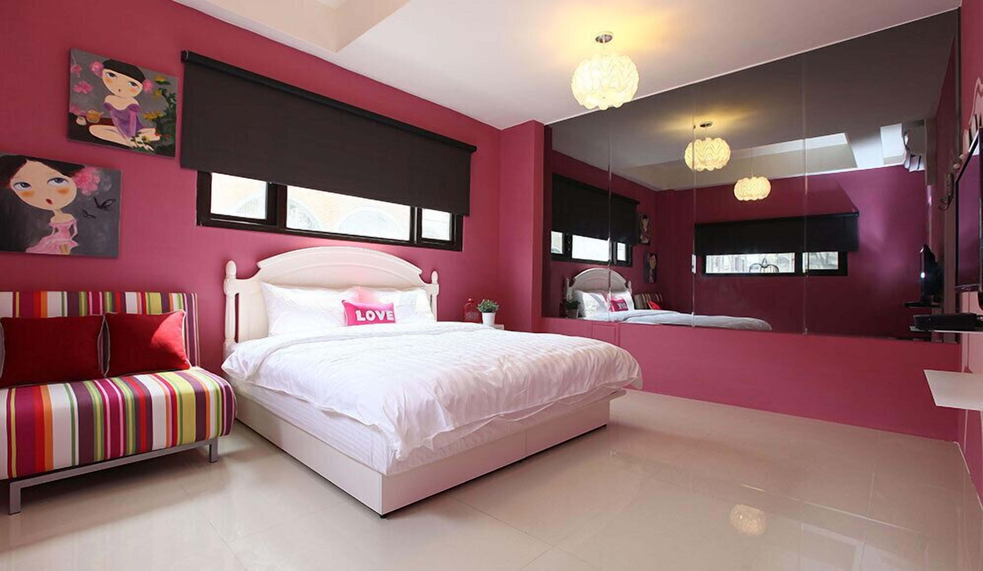 Quarto com cama grande, mesa de cabeceira, sofá listrado e espelho.