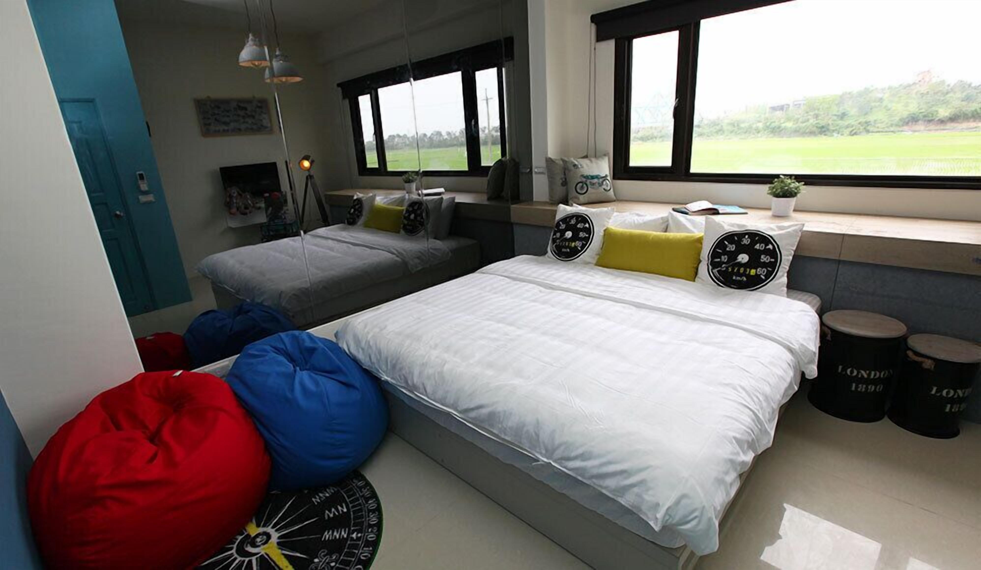 A modern bedroom with a large bed, two smaller beds, bean bags, and a view of a green field.