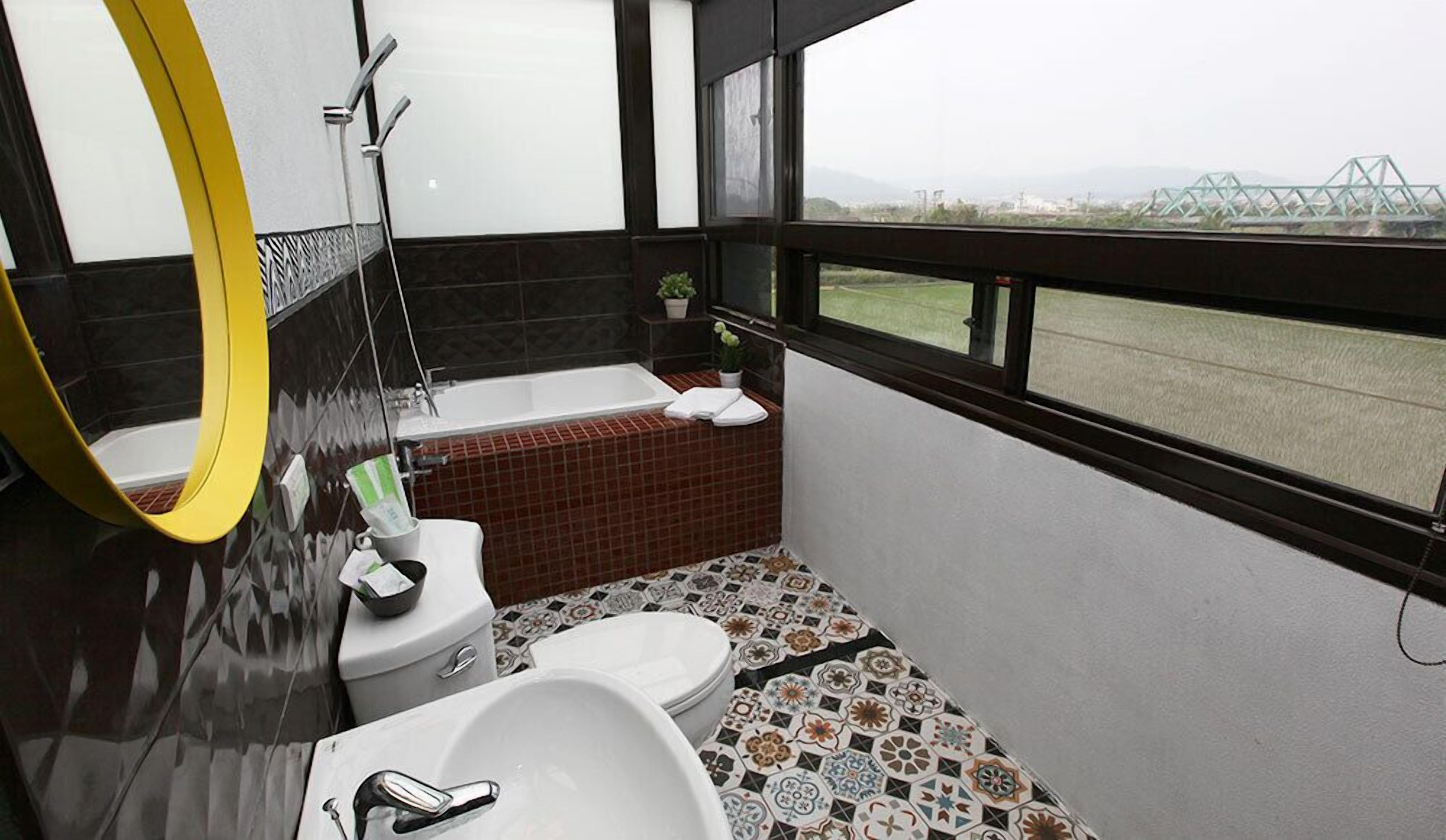 A bathroom with a bathtub, toilet, and sink. There is a window with a view of a bridge and greenery.