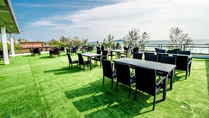 An outdoor patio with tables and chairs, a view of the sea, and a building in the background. - Hai Ma Hotel (Sihanoukville)