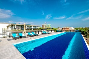 A swimming pool with lounge chairs, a building with a glass facade, and a construction crane in the background.