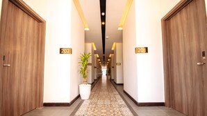 A hotel corridor with wooden doors numbered 202 and 201, a patterned carpet, and a potted plant. - Hai Ma Hotel (Sihanoukville)