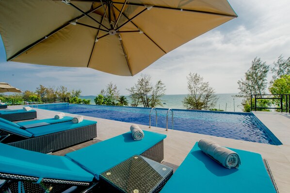 A poolside area with lounge chairs and a large umbrella, overlooking a body of water.