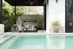 Relax by the serene pool surrounded by lush greenery and a shaded deck.