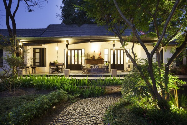 Enjoy al fresco dining on the covered patio surrounded by lush greenery and a stone pathway.