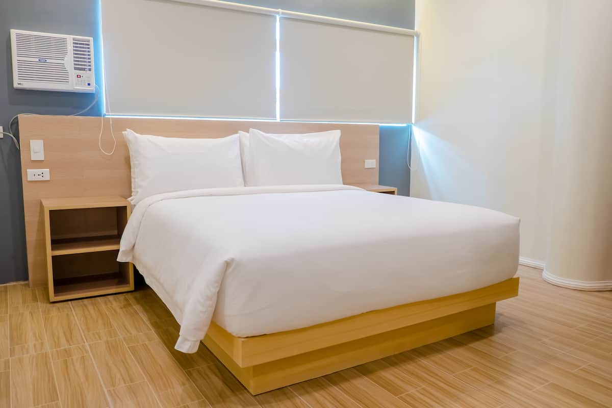 A modern hotel room with a wooden bed frame, white bedding, and a built-in shelf.