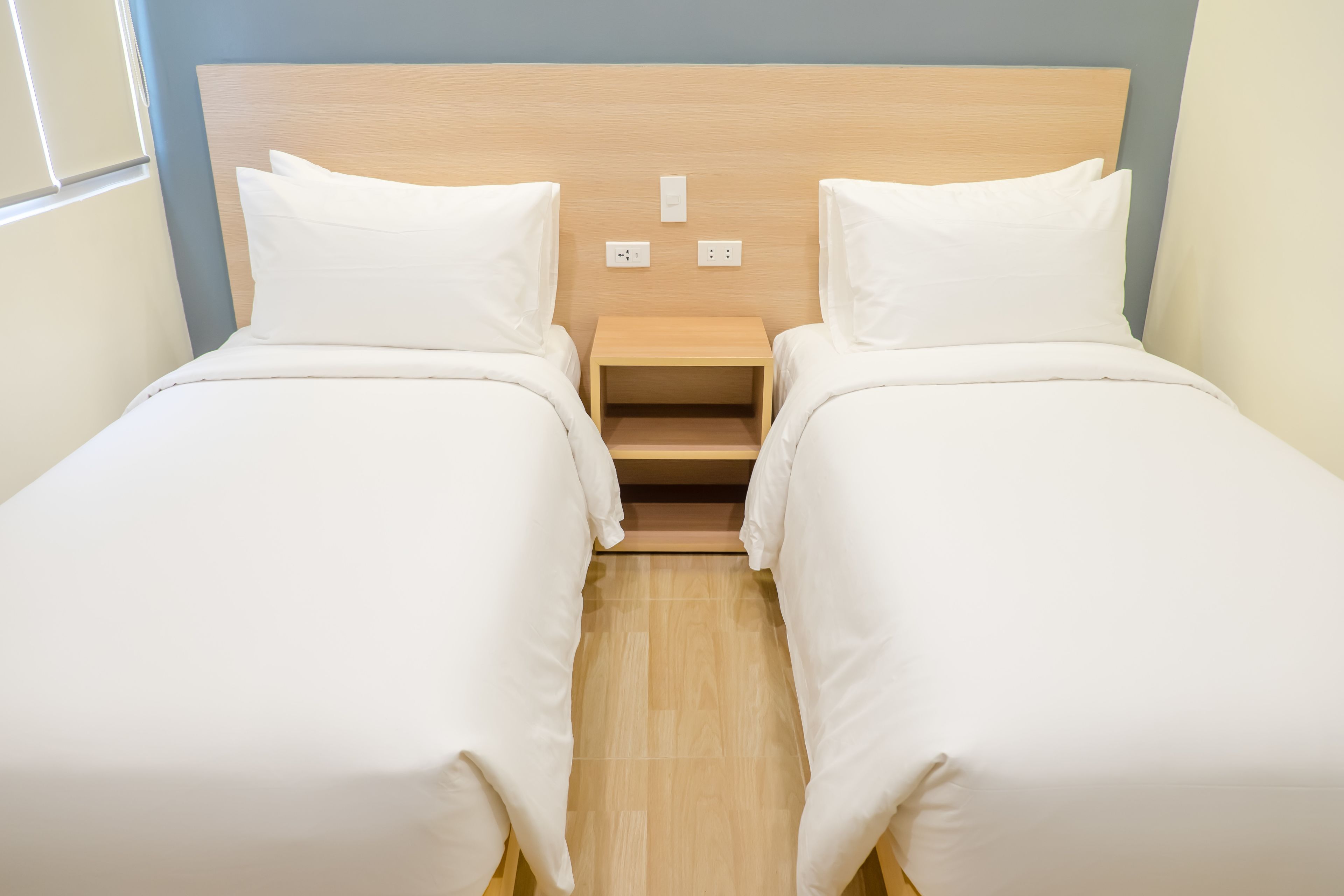 A twin room with two single beds, a wooden headboard, bedside tables, and a small shelf.