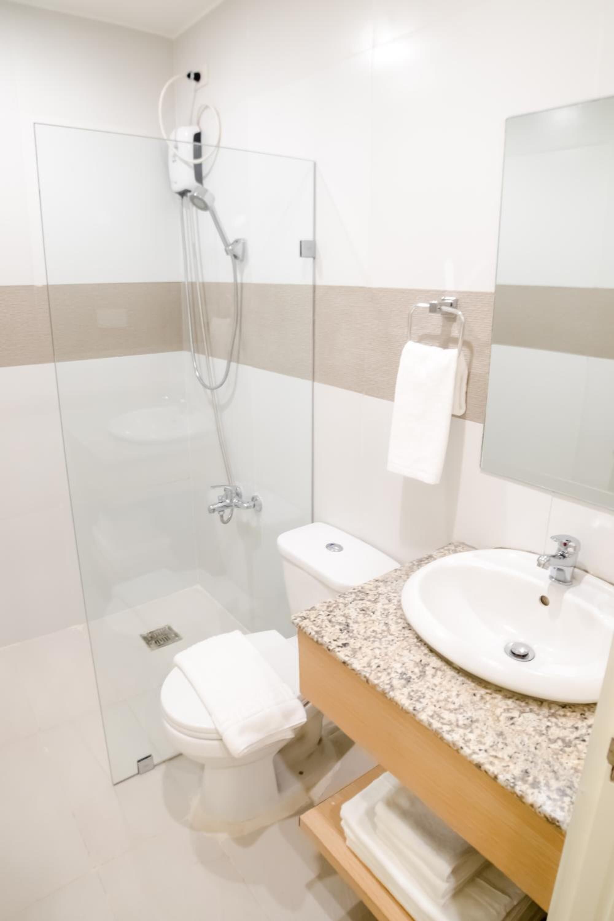 A modern bathroom with a glass-enclosed shower, a white toilet, a granite countertop sink, and a mirror.