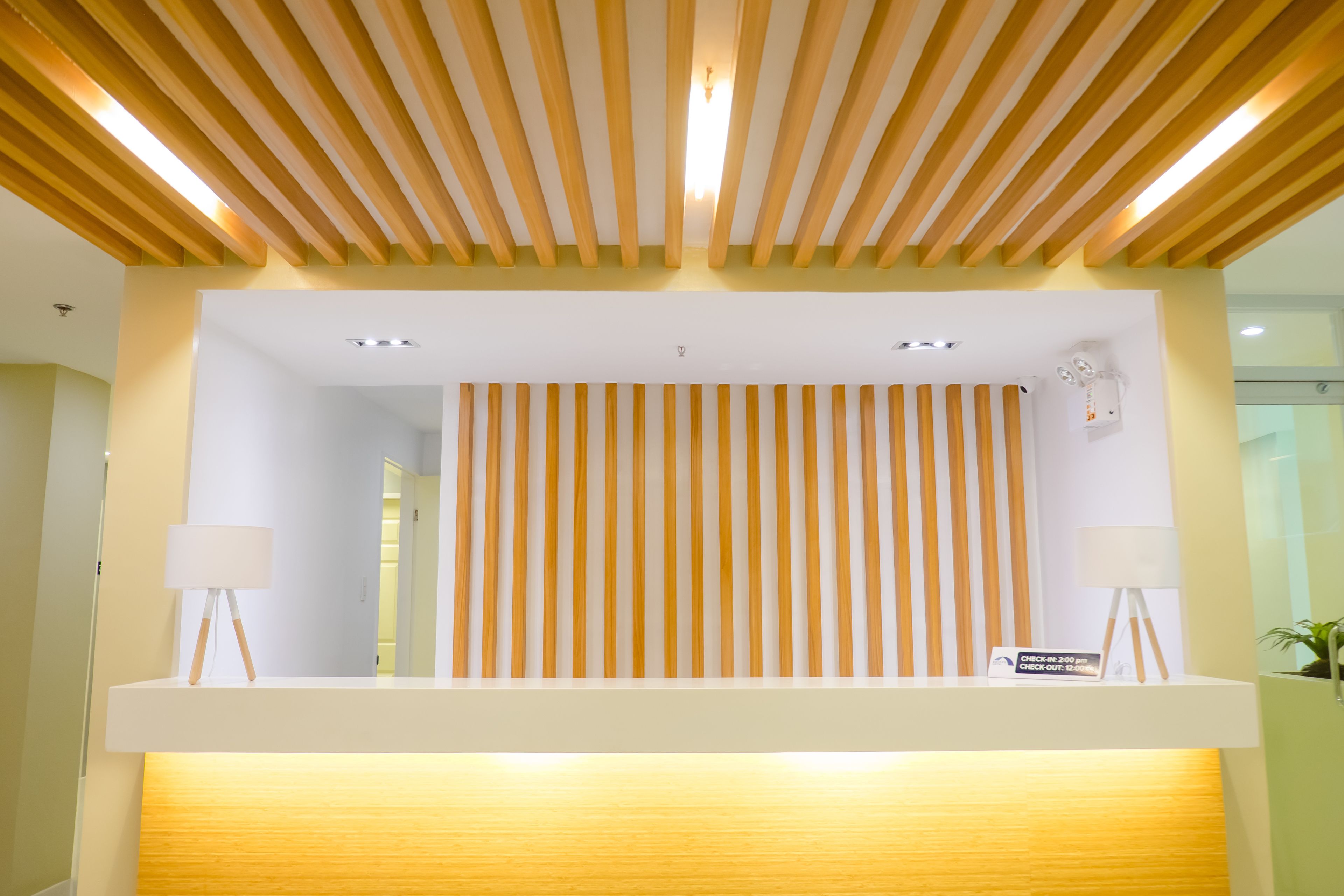A reception desk with a wooden slatted ceiling, a vertical striped wall, and two floor lamps.