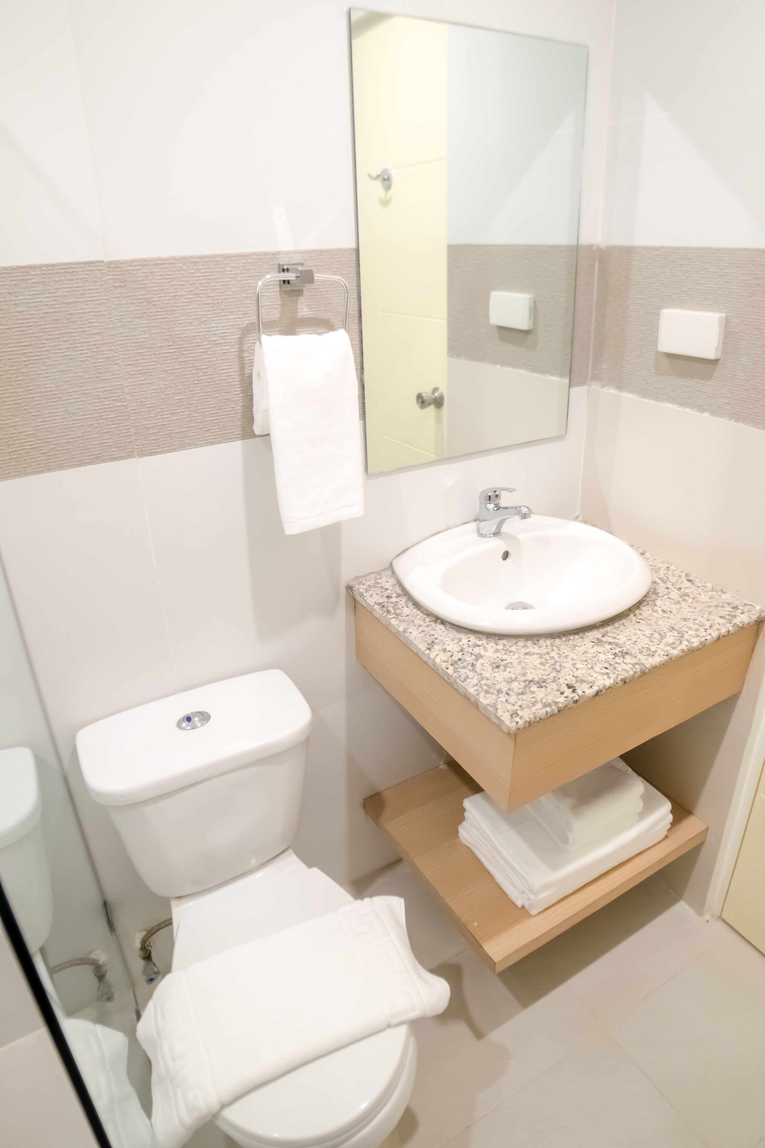 Un baño con inodoro blanco, lavamanos con encimera de granito y espejo sobre el lavamanos.