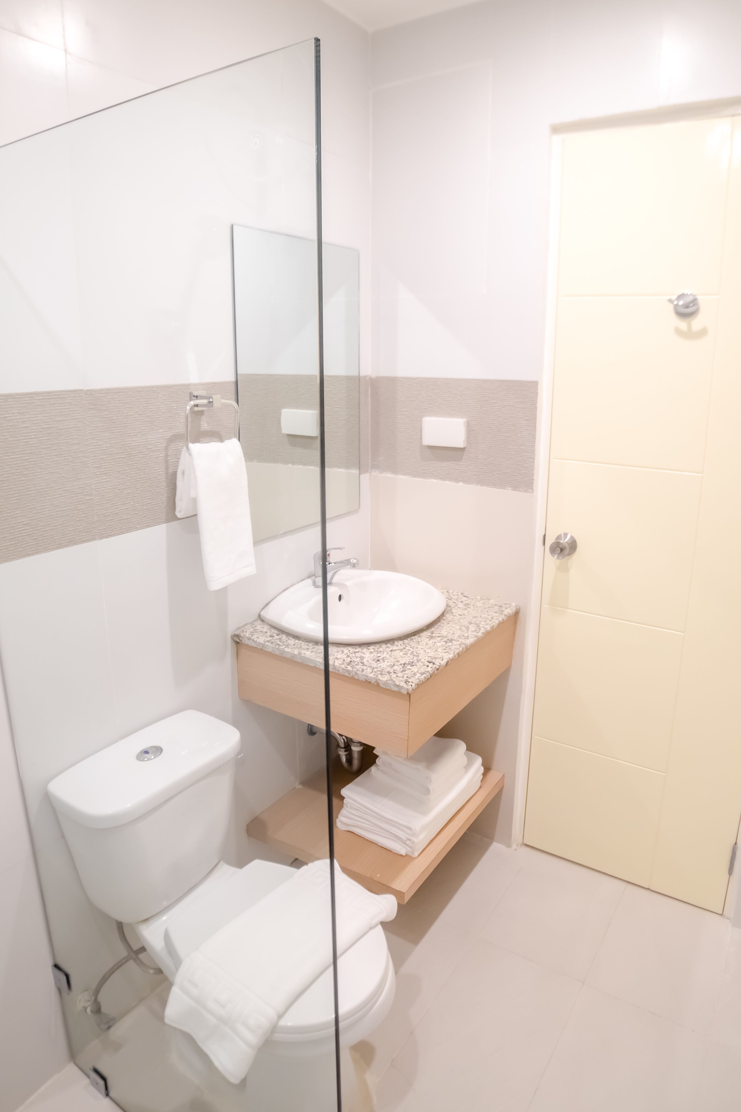 A modern bathroom with a glass shower enclosure, a white toilet, a sink with a granite countertop, and a beige door.