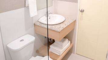 A modern bathroom with a glass shower enclosure, a white toilet, a sink with a granite countertop, and a beige door.