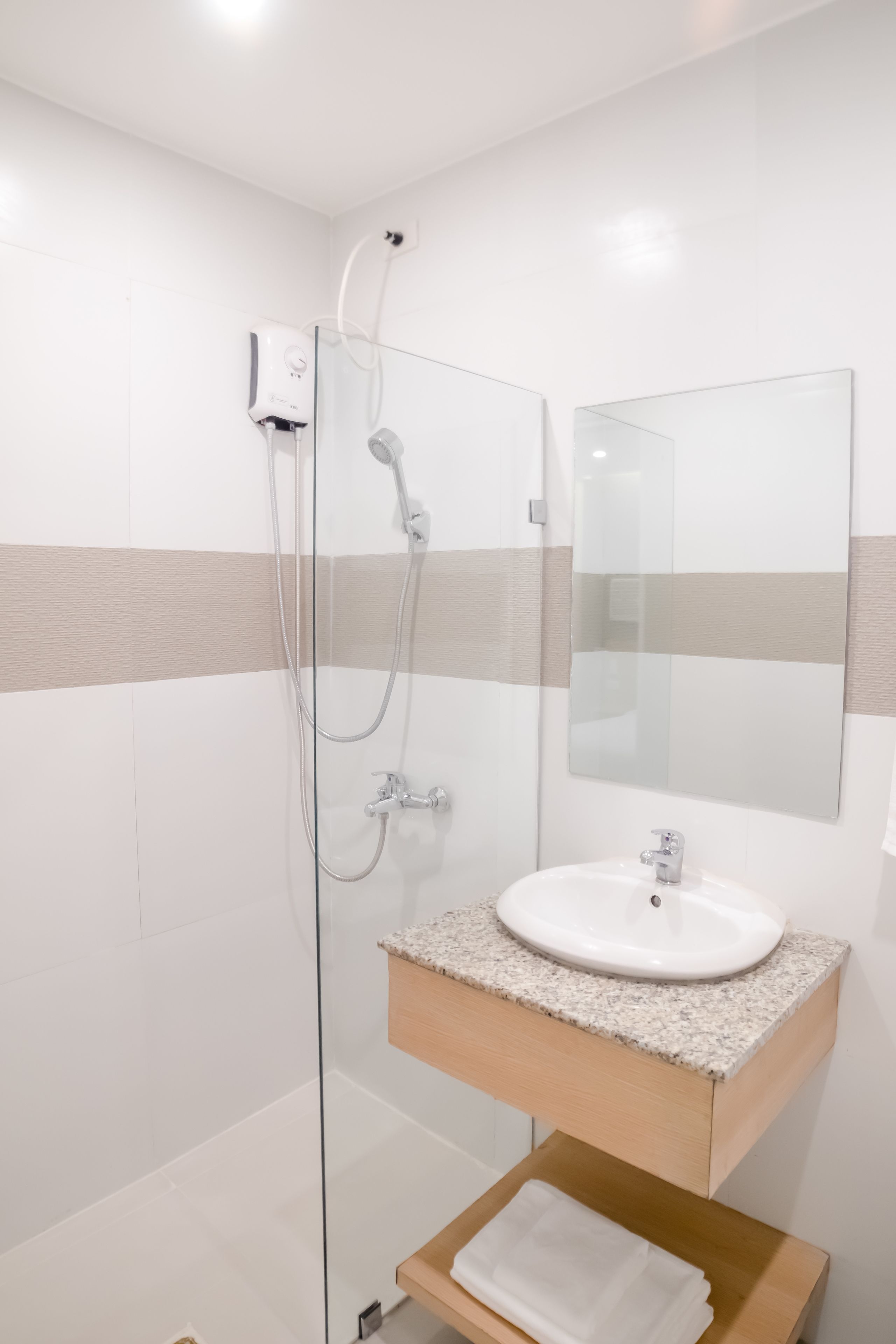 Un baño moderno con cabina de ducha de vidrio, un lavamanos blanco y encimera de granito, y un mueble de tocador de madera.