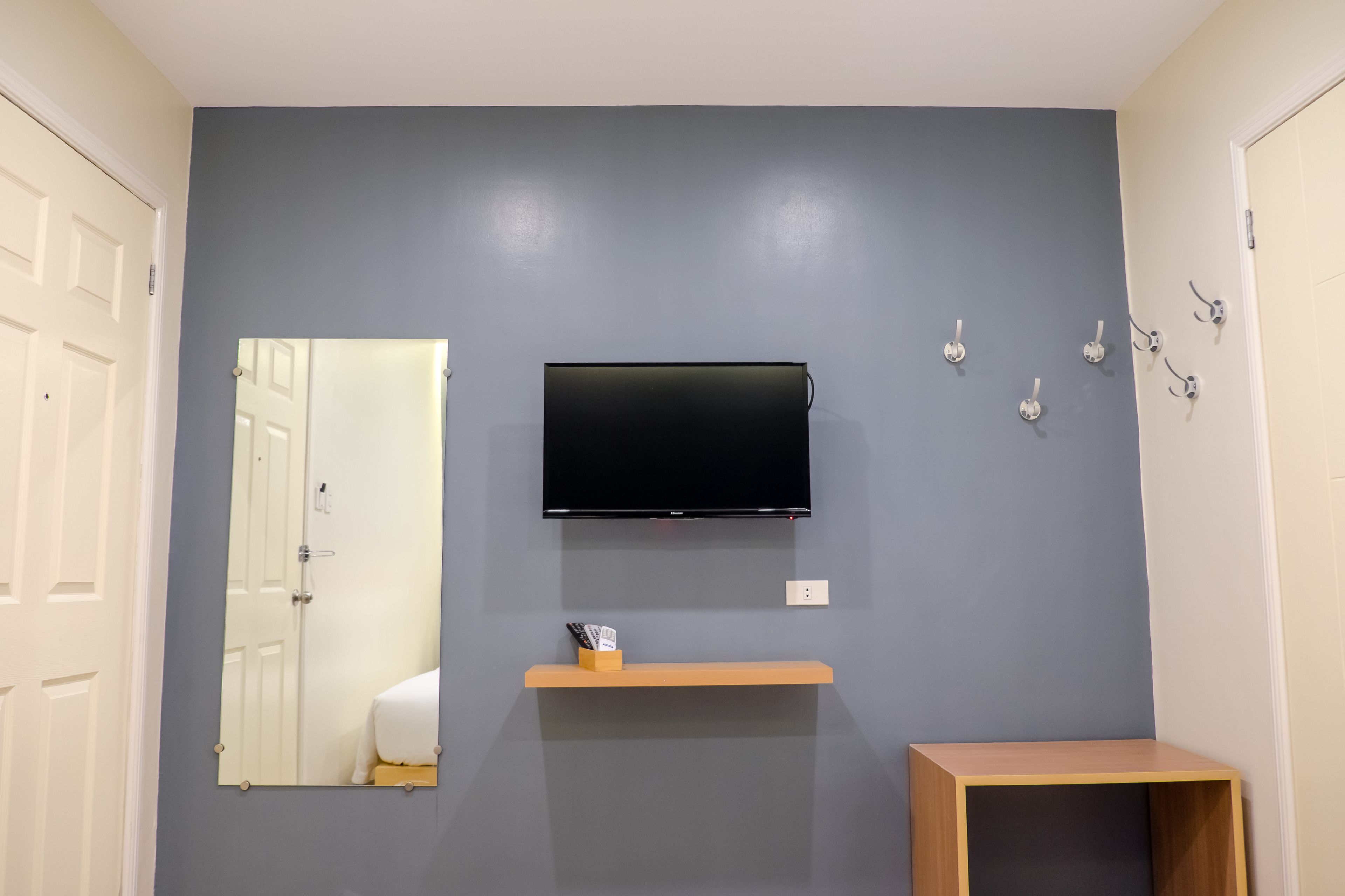 Une pièce dotée d’un téléviseur à écran plat fixé au mur, d’une étagère en bois en dessous et d’une petite table en bois sur le côté droit.