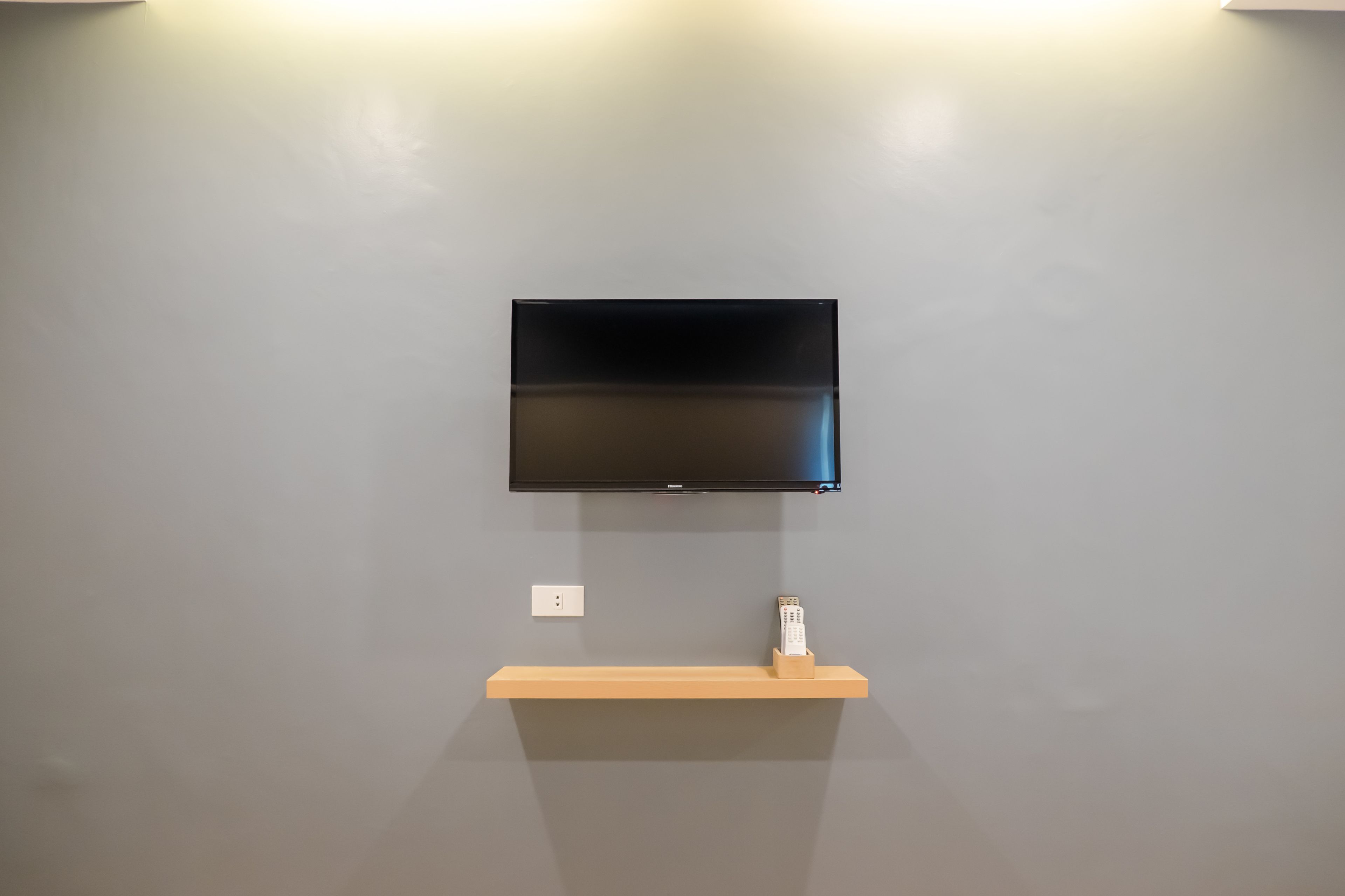 A flat-screen TV mounted on a gray wall with a wooden shelf below it.