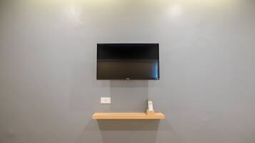 A flat-screen TV mounted on a gray wall with a wooden shelf below it.