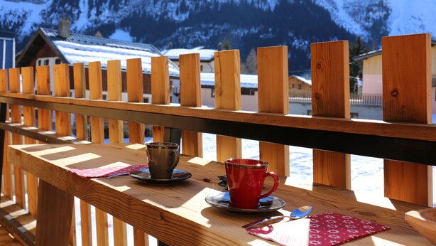 En träveranda med utsikt över snöklädda berg och en stuga i bakgrunden.