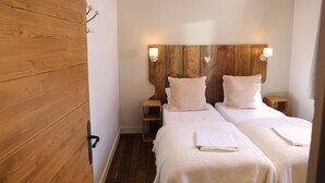 Ett hotellrum med två sängar, sänggavel i trä, sängbord och väggmonterade lampor.