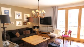 Ett vardagsrum med en soffa, ett soffbord, en tv, en kristallkrona och en skjutdörr i glas som leder ut till uteplatsen.