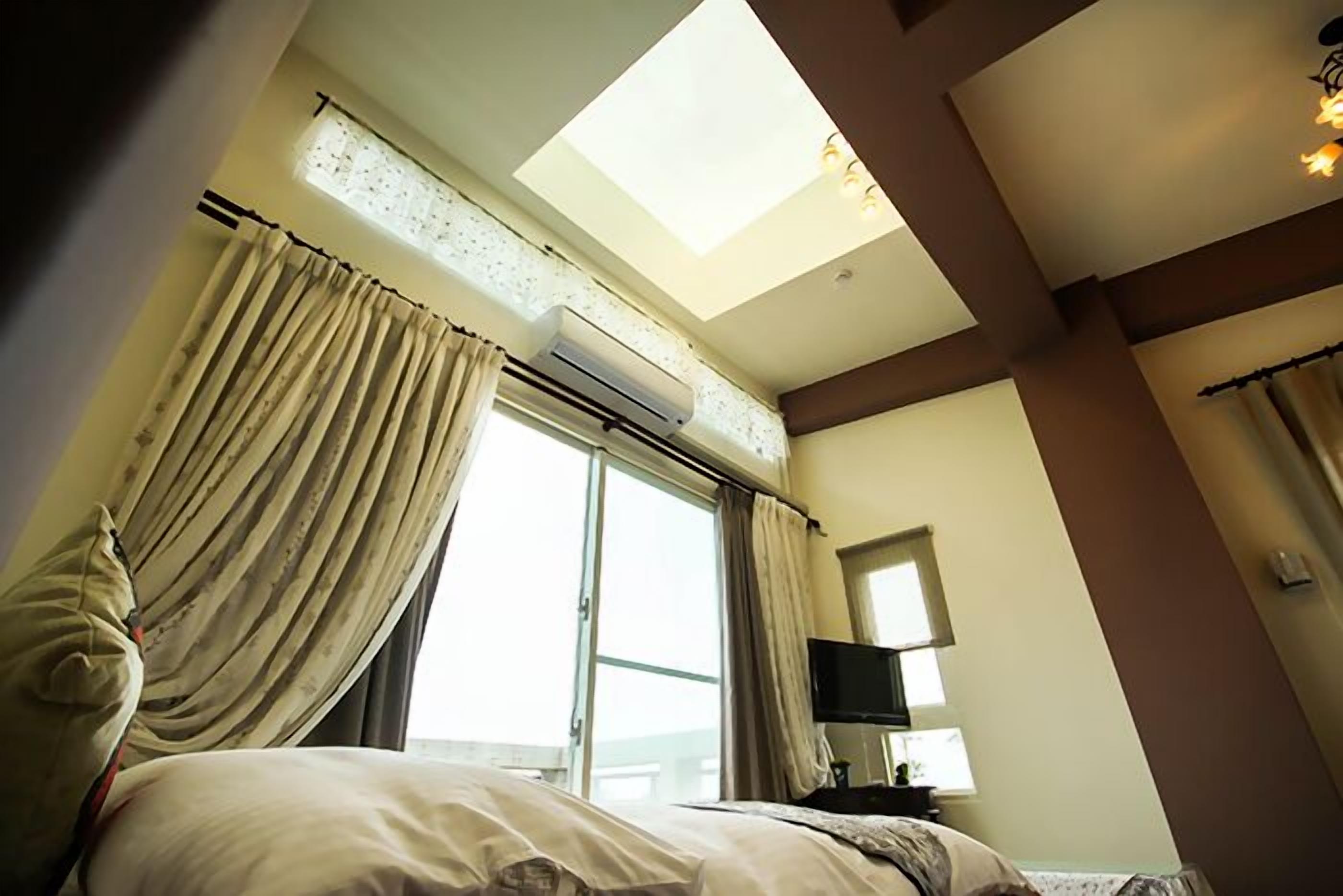 A hotel room with a skylight, a bed, curtains, a flat-screen TV, and a window.
