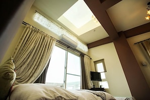 A hotel room with a skylight, a bed, curtains, a flat-screen TV, and a window.