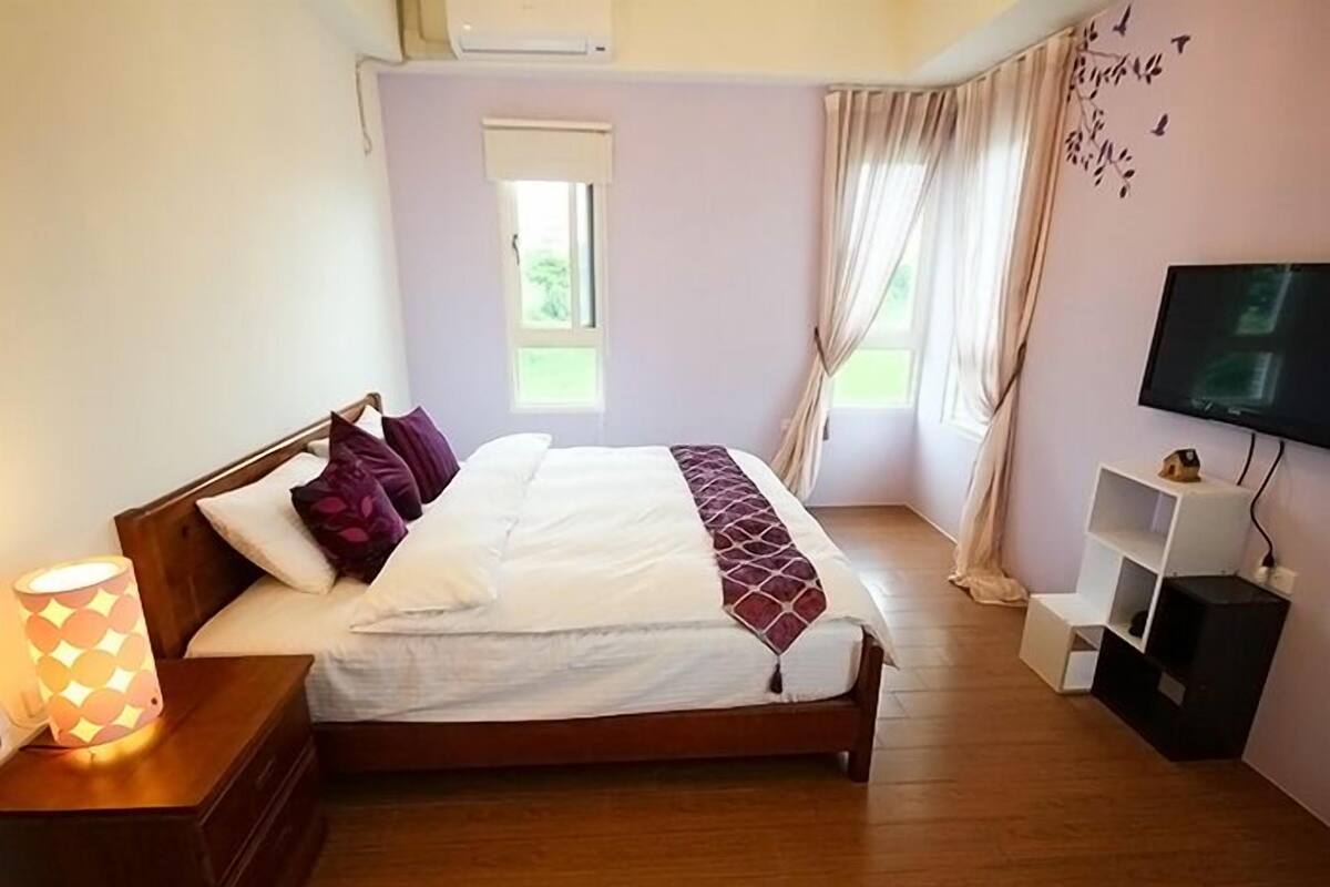 Un dormitorio con cama, televisión, mesita de noche y ventana.
