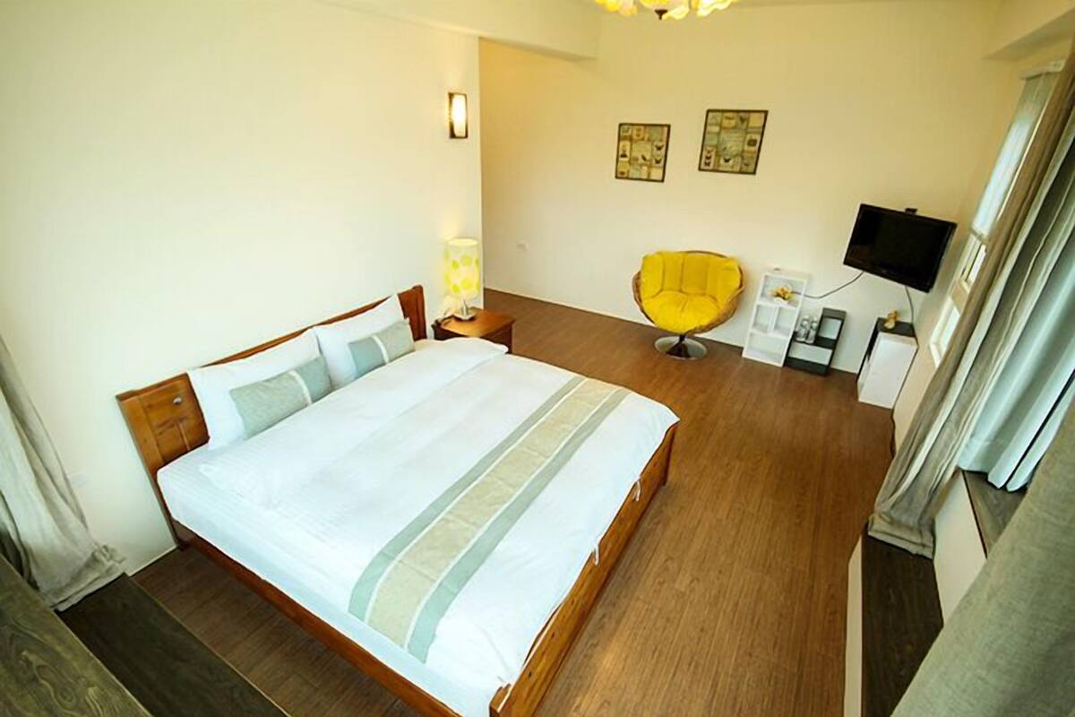 Un dormitorio ordenado con una cama grande, una silla, un televisor y una mesita de noche.