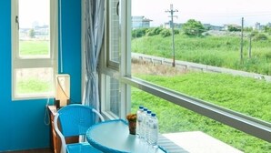 Een balkon met een blauwe stoel, een klein tafeltje en uitzicht op een groen veld en weg.