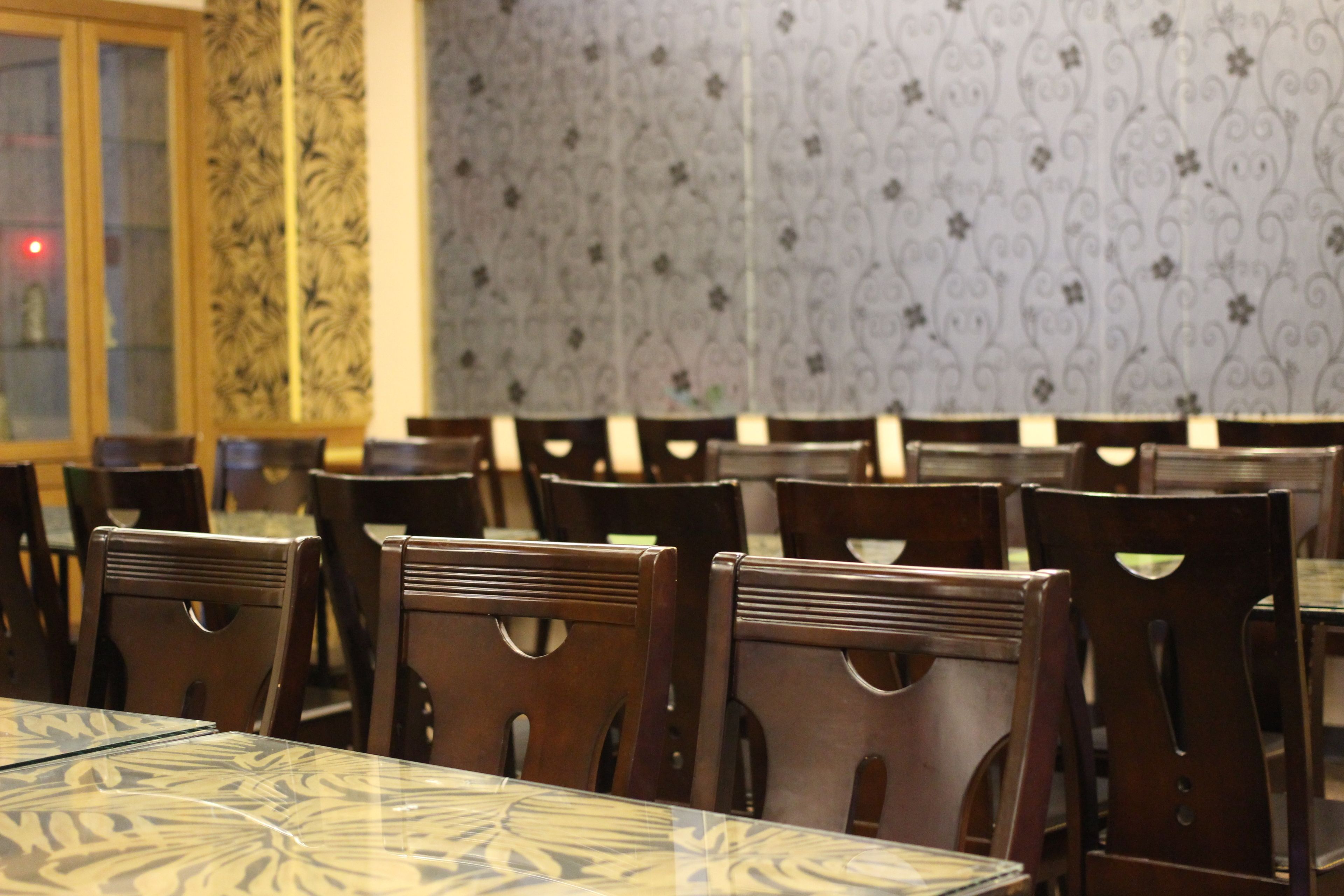 A dining area with wooden chairs and tables, patterned wallpaper, and a window with a view.