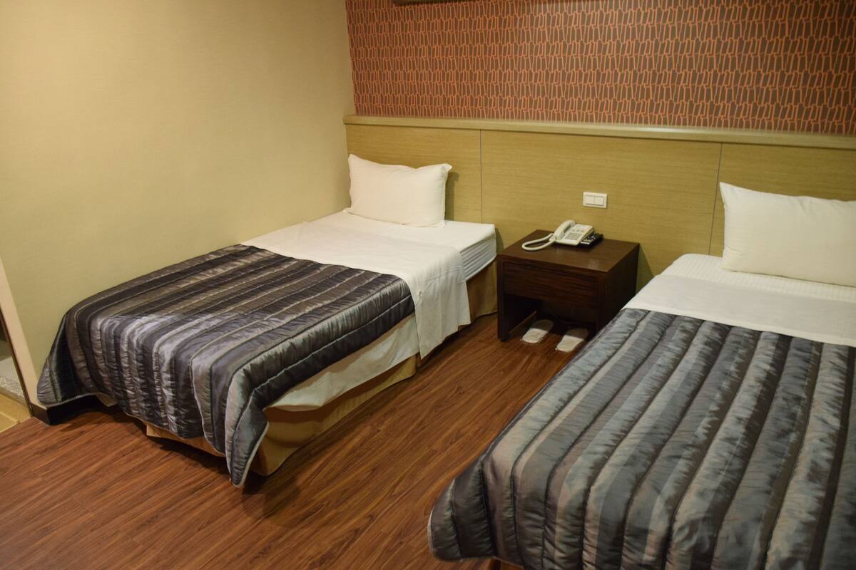 A hotel room with two beds, wooden flooring, a patterned headboard, and a bedside telephone.