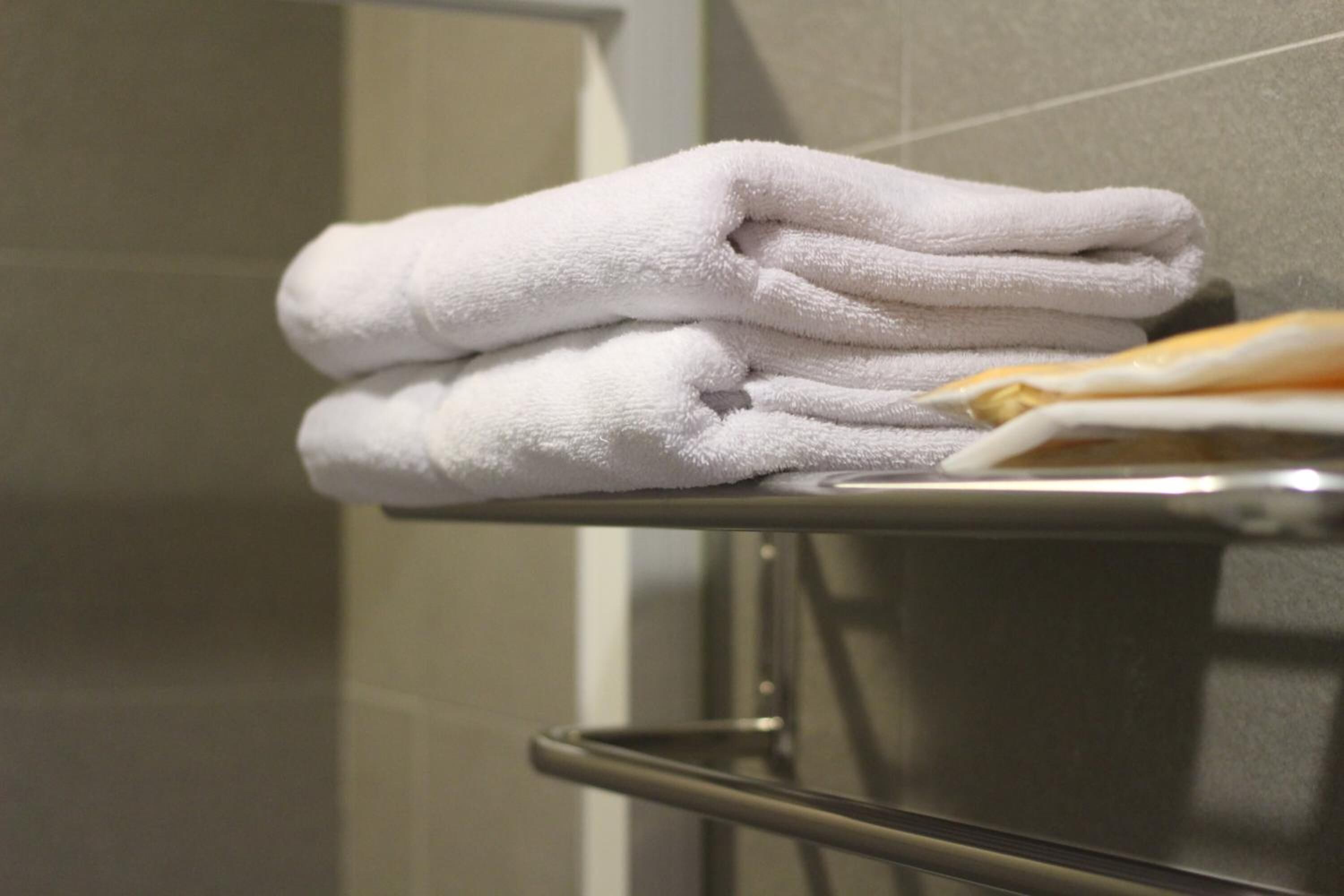 Un montón de toallas blancas sobre una repisa metálica en un baño.