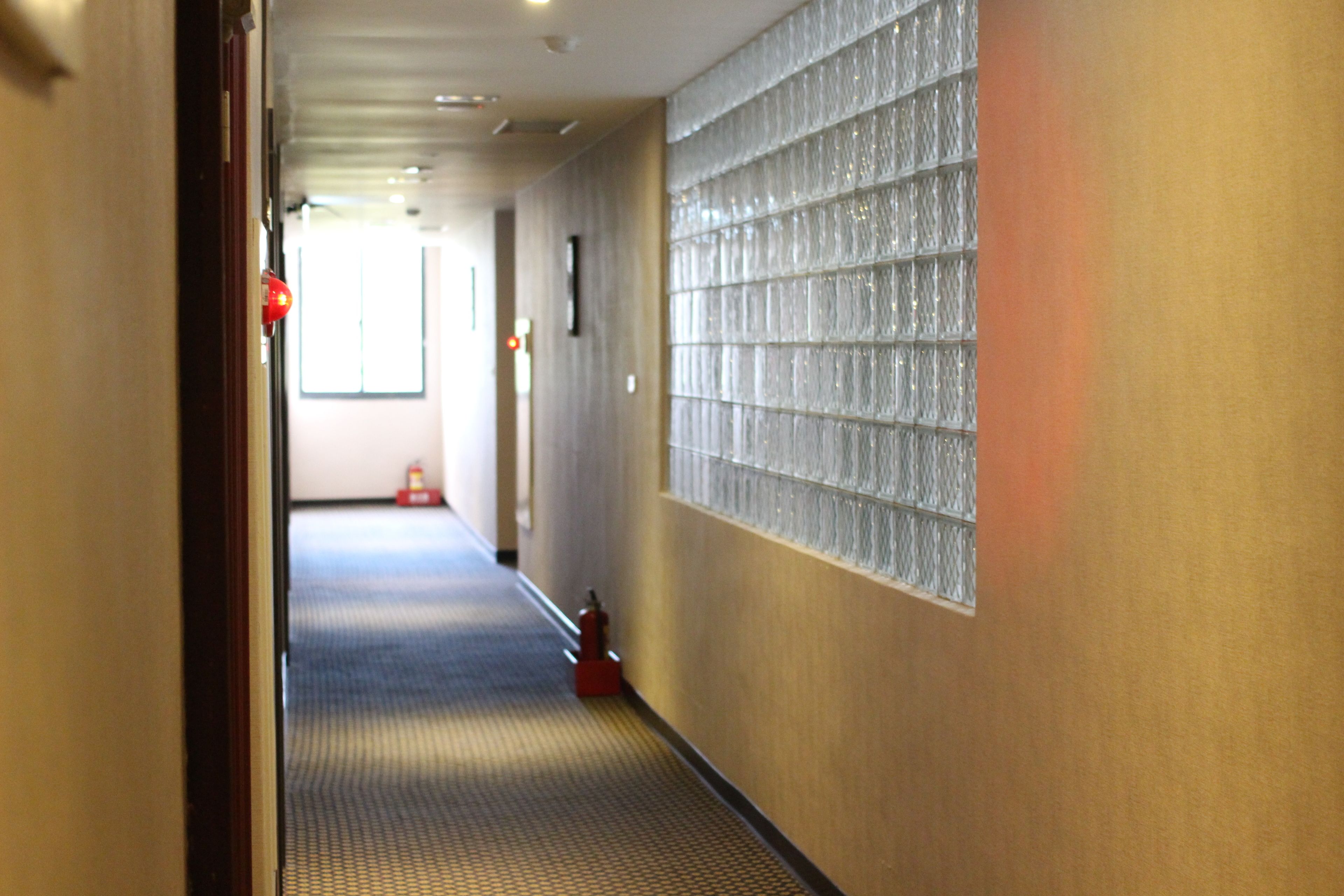 Un pasillo con pared texturizada, un extintor y una puerta a la izquierda.