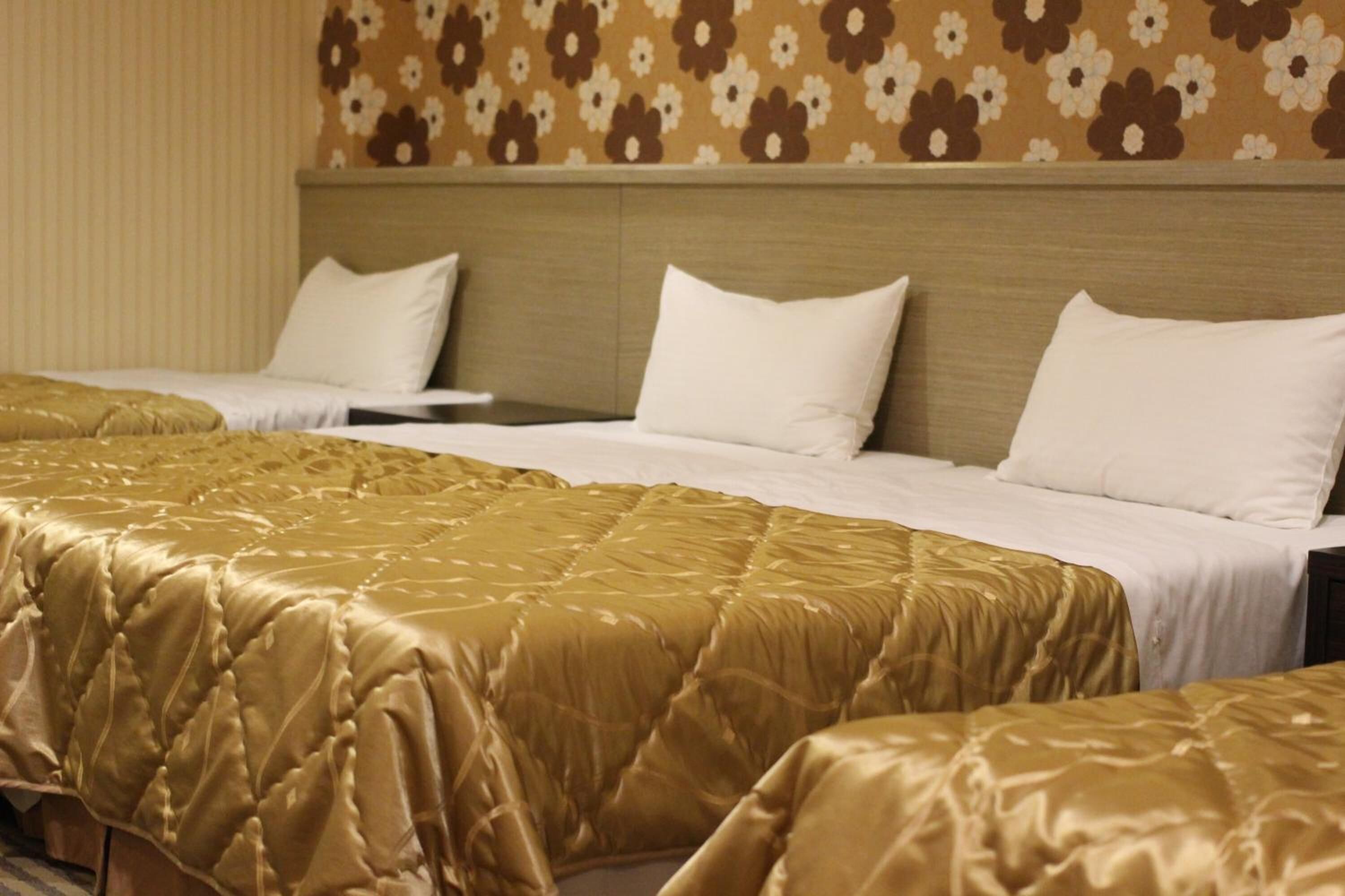 Ein Hotelzimmer mit zwei Betten, jeweils mit einer goldenen und weißen Bettdecke. Das Zimmer hat einen floralen Wandbelag und ein hölzernes Kopfteil.