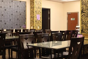 A conference room with multiple tables and chairs, a patterned wall, and a door with an exit sign. - Home Full Hotel (Jincheng)