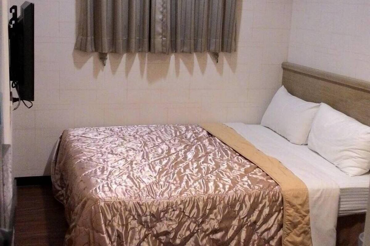 A hotel room with a bed, a window with curtains, an air conditioning unit, and a framed picture on the wall.