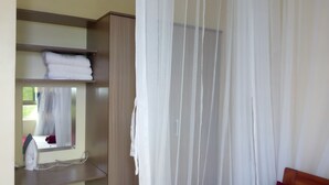 A bedroom with a bed, a wardrobe, a mirror, and a window with sheer curtains. - Sunset Paradise Baringo 11 (Shanzu)