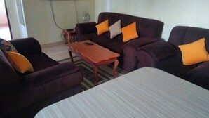 A living room with a sofa set, a coffee table, and a flat-screen TV mounted on the wall. - Sunset Paradise Baringo 11 (Shanzu)
