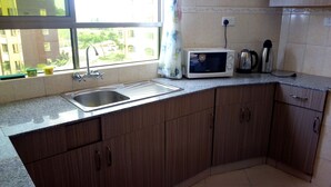 A kitchen with a stainless steel sink, a microwave, and a kettle on the countertop. - Sunset Paradise Baringo 11 (Shanzu)
